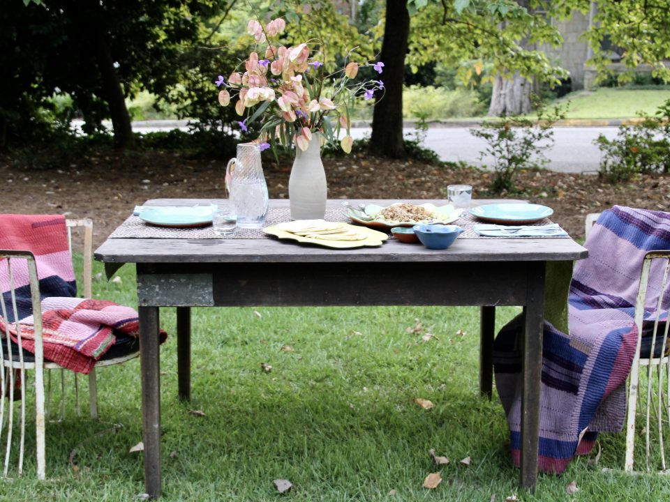Table set up with Rebecca Wood dinnerware, outside, and chairs covered in Aloka quilts.